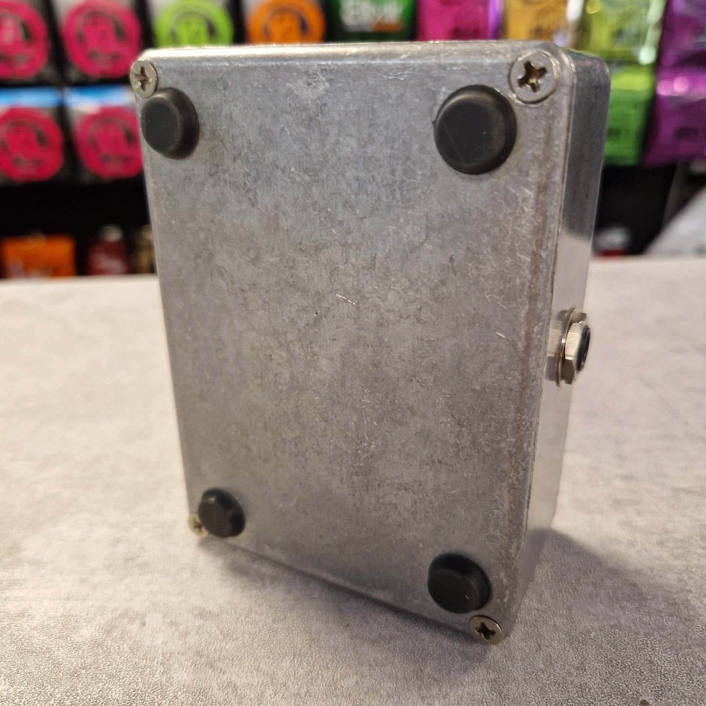 Pre-Owned Guild Brian May Metal box with screws on a gray surface with colorful objects in the background