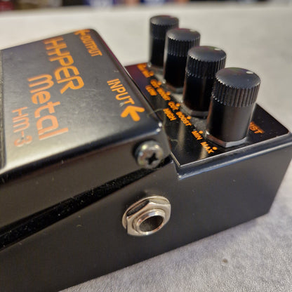 Pre-Owned Boss HM-3 Guitar effects pedal with 'Hyper Metal' branding on a blurred background