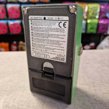Pre-Owned Ibanez TS9 Battery pack with label on a gray surface, colorful items in the background