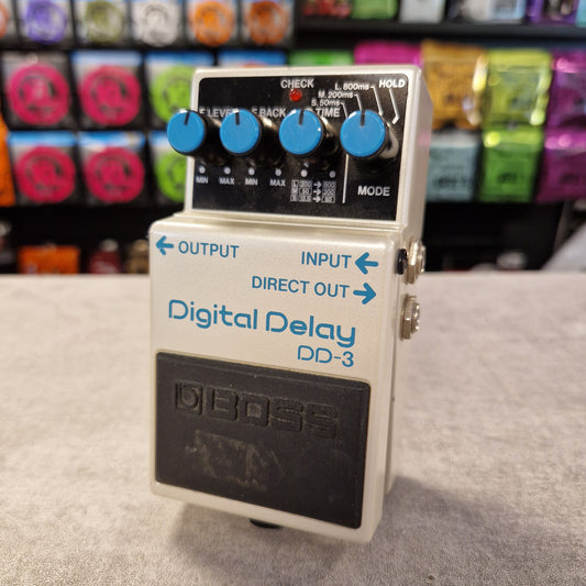 Pre-Owned Boss DD-3 Boss Digital Delay DD-3 guitar effects pedal on a gray surface with colorful equipment in the background.