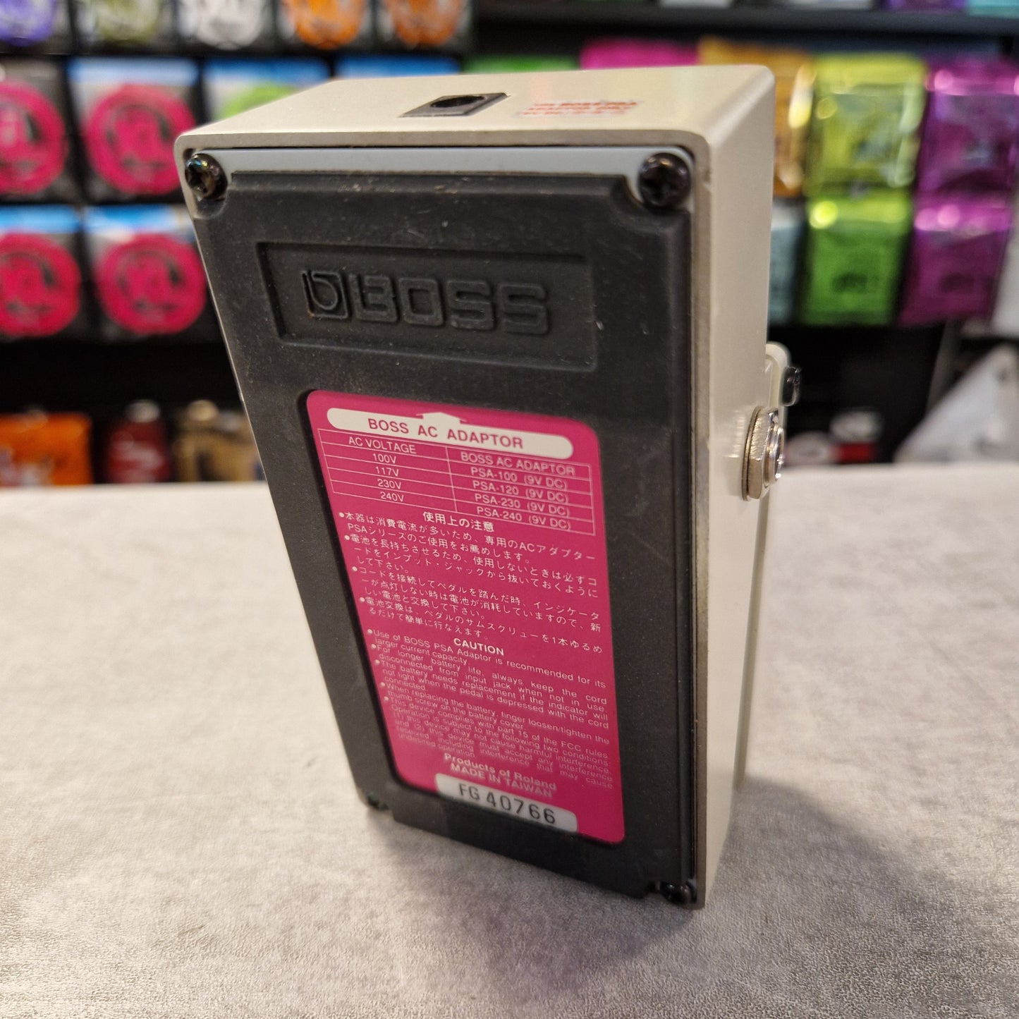 Pre-Owned Boss DD-3 Electrical box with a red label on a wall, with colorful objects in the background.