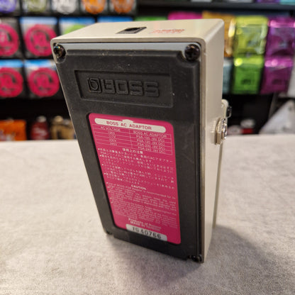Pre-Owned Boss DD-3 Electrical box with a red label on a wall, with colorful objects in the background.