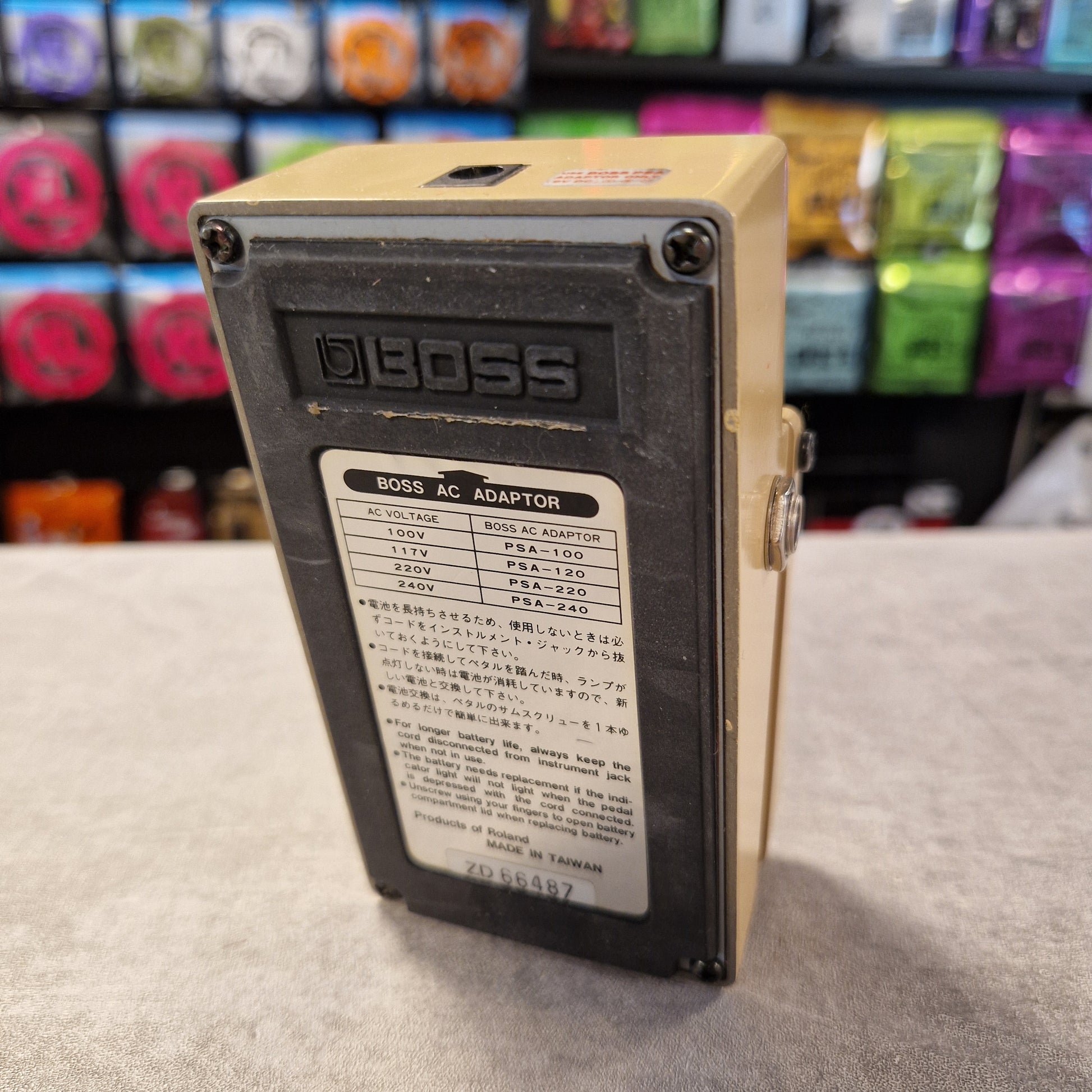 Pre-Owned Boss AW-2 Boss AC adapter with specifications on a gray surface, colorful items in the background