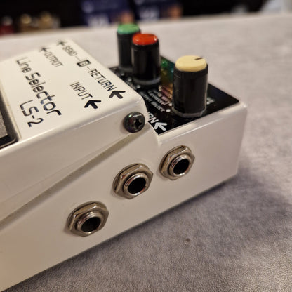 Pre-Owned Boss LS-2 Close-up of a Line Selector LS-2 device with knobs and ports on a gray surface.