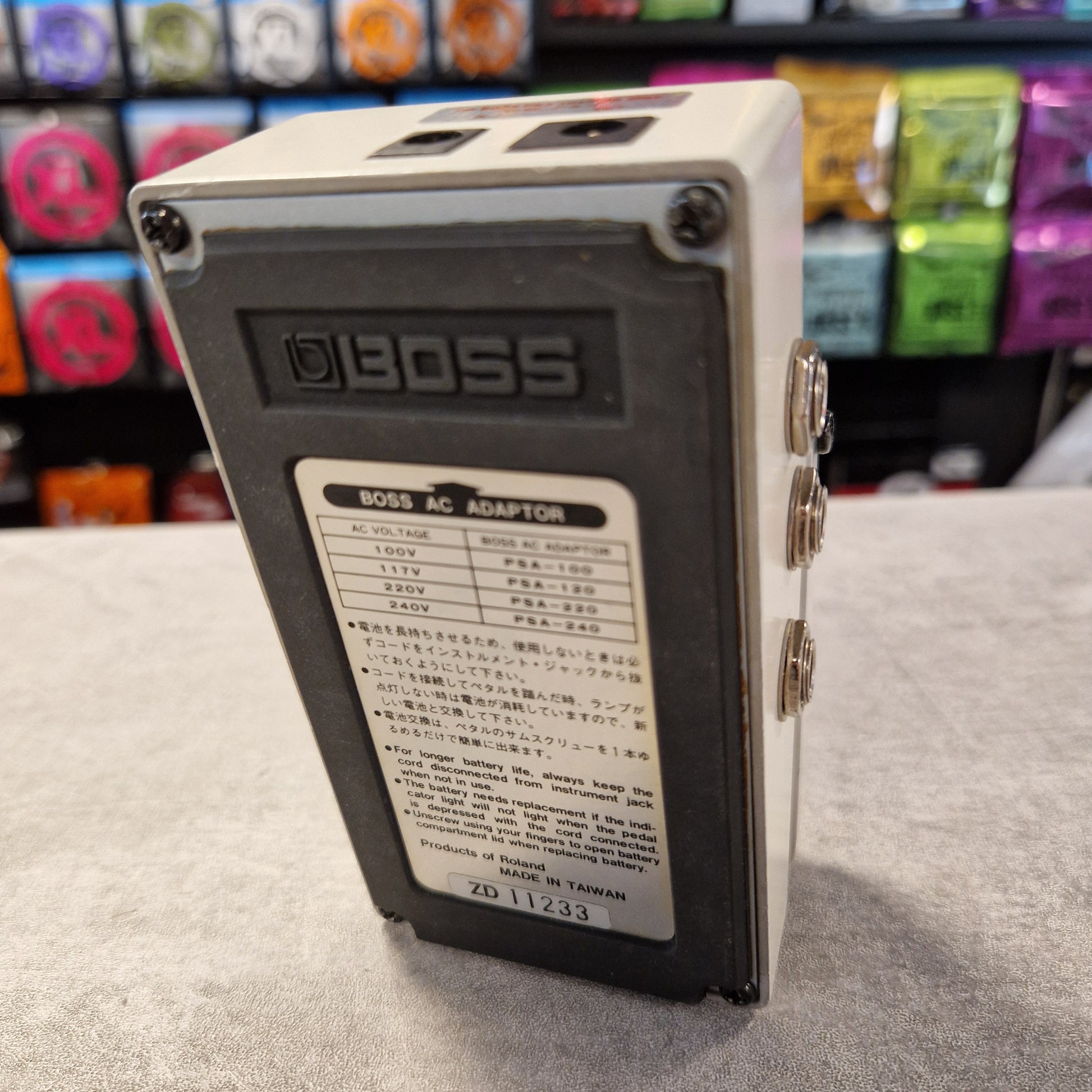 Pre-Owned Boss LS-2 BOSS AC adapter on a gray surface with colorful items in the background