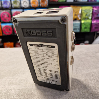 Pre-Owned Boss LS-2 BOSS AC adapter on a gray surface with colorful items in the background