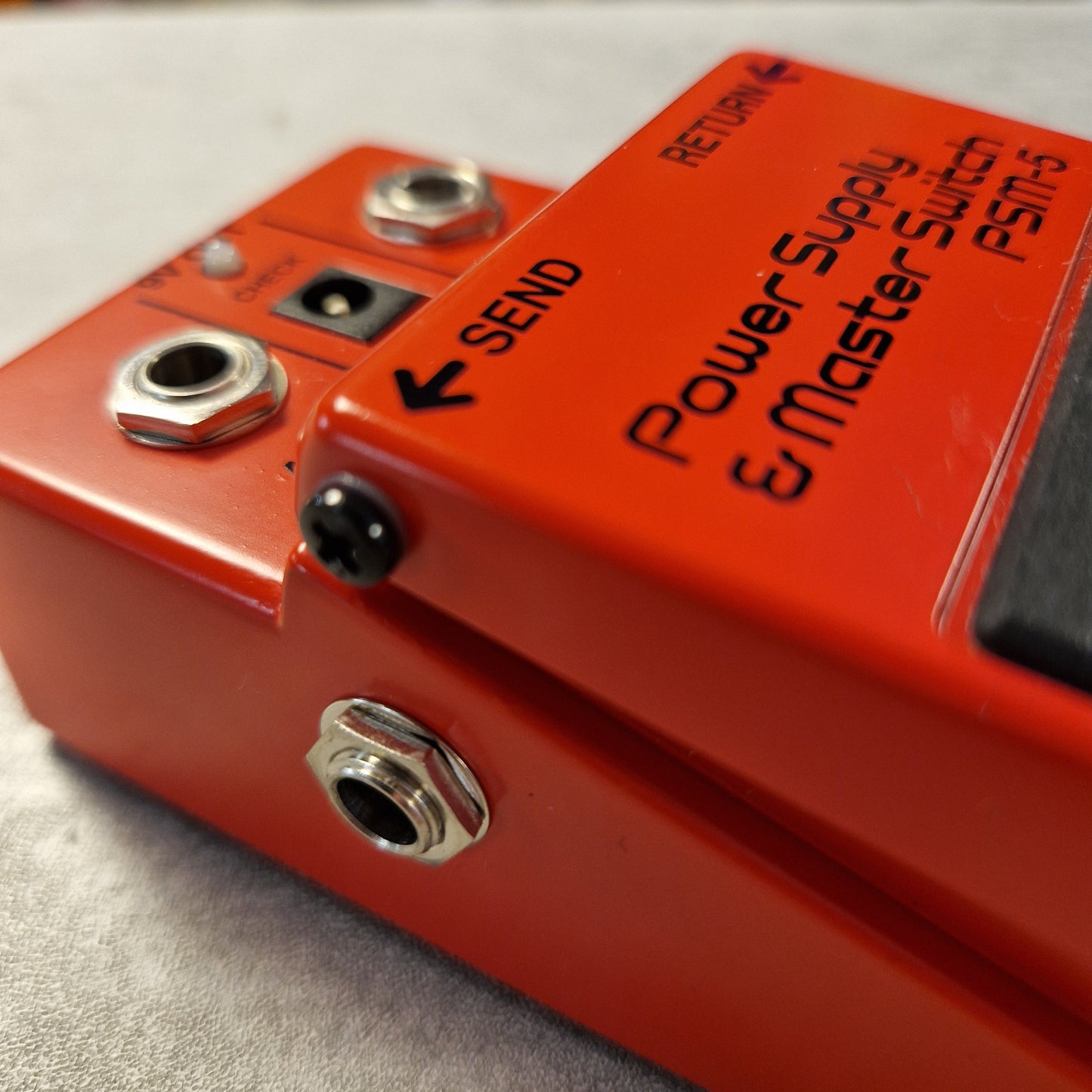 Pre-Owned Boss PSM-5 Close-up of a red electronic pedal with labeled ports on a metallic surface.