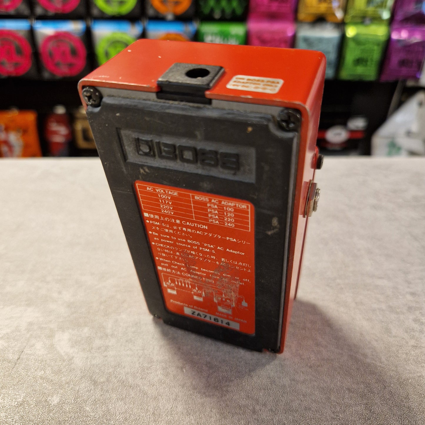 Pre-Owned Boss PSM-5 Red and black electronic device on a textured surface with colorful boxes in the background