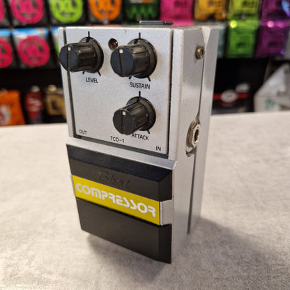 Pre-Owned Tokai TCO-1 Compressor pedal with knobs on a gray surface, colorful pedals in the background