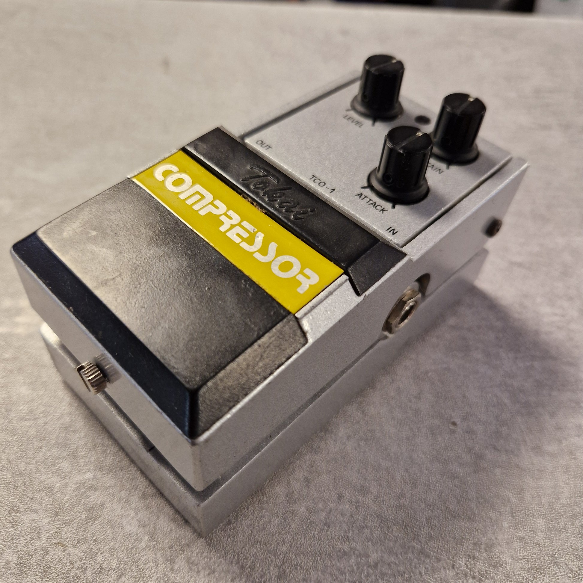 Pre-Owned Tokai TCO-1 Compressor pedal with a yellow label on a gray surface