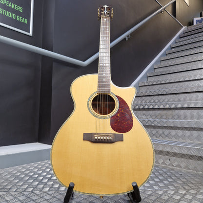 Pre-Owned Crafter TMC035/N Acoustic guitar on a stand in front of a staircase with a dark wall and metal railing.