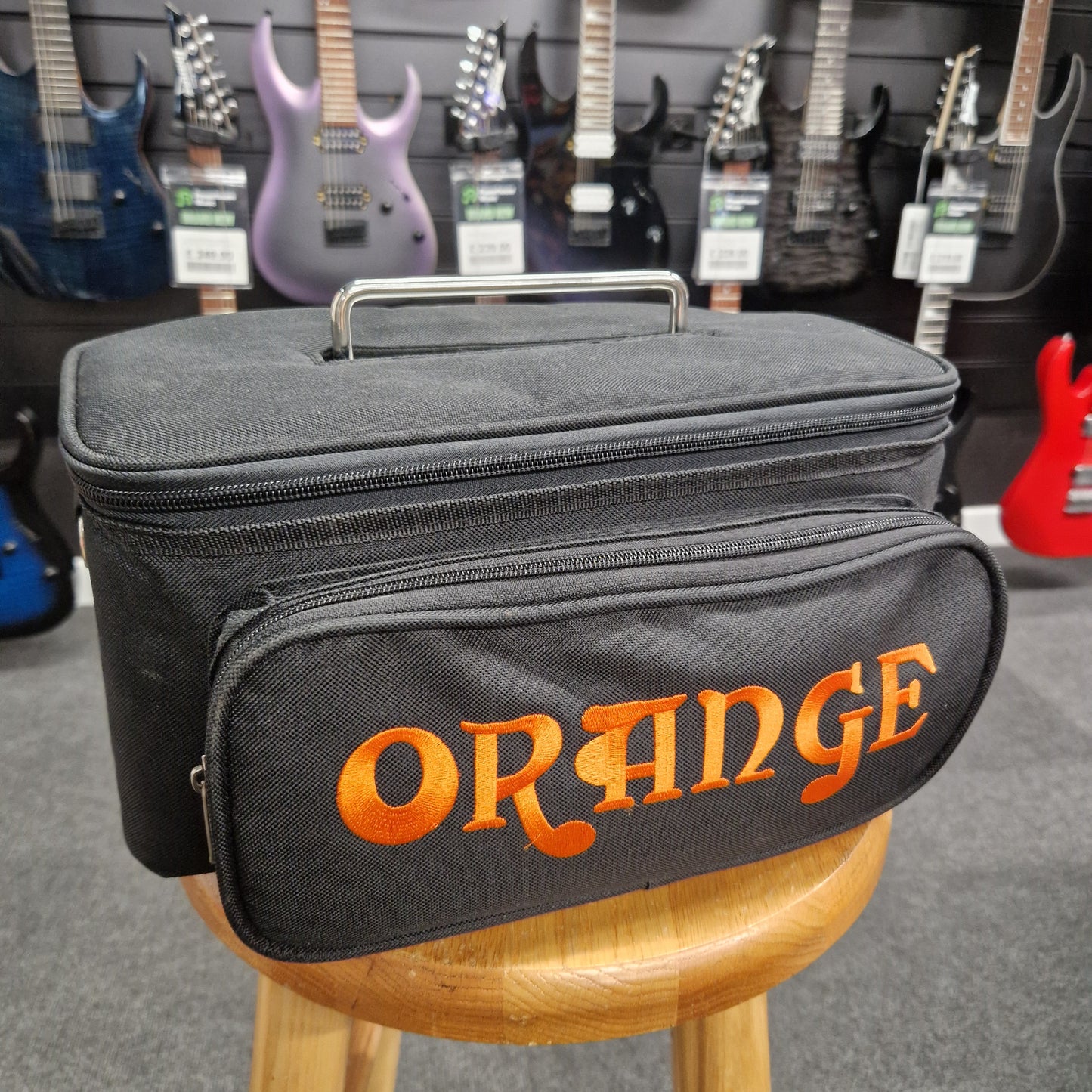 Pre-Owned Orange TT15H Black guitar case with 'Orange' branding in an indoor setting with guitars in the background