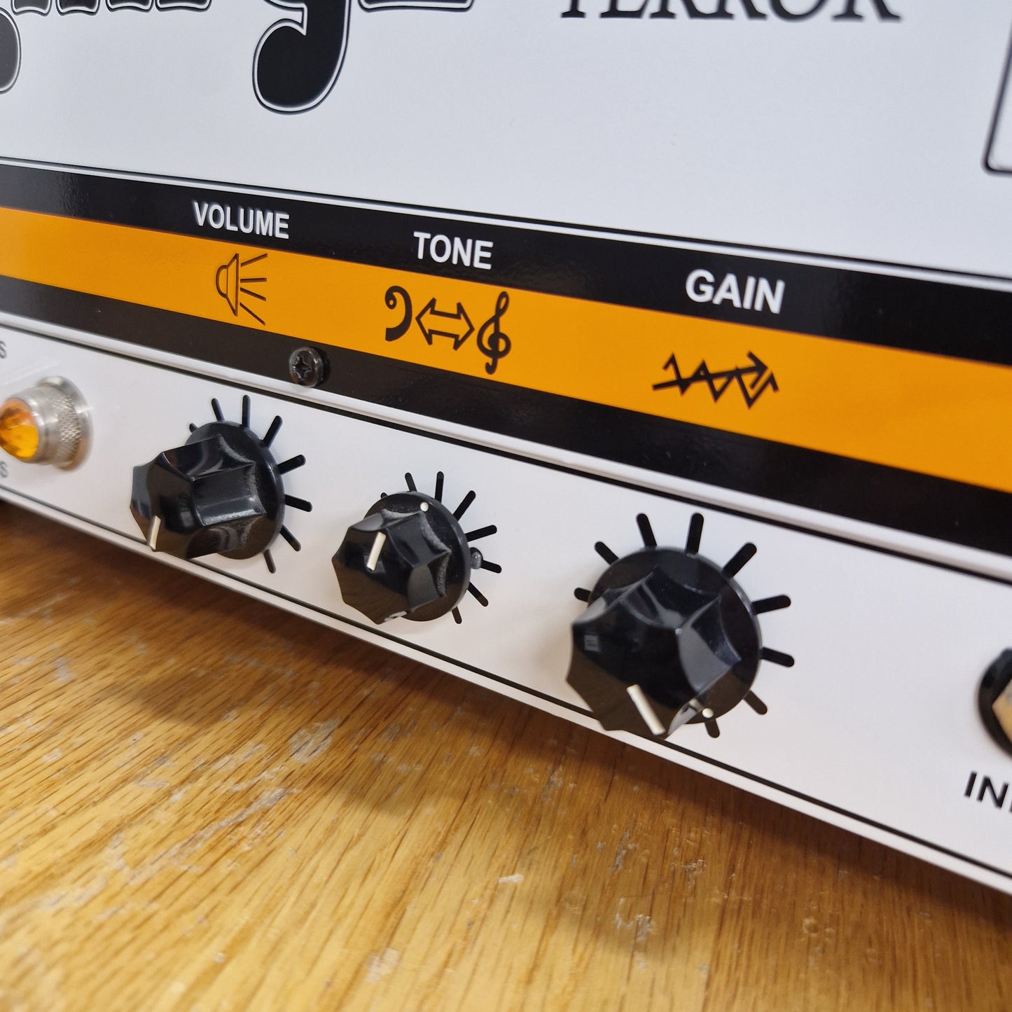 Pre-Owned Orange TT15H Close-up of a guitar effects pedal with knobs labeled Gain, Tone, and Volume on a wooden surface.
