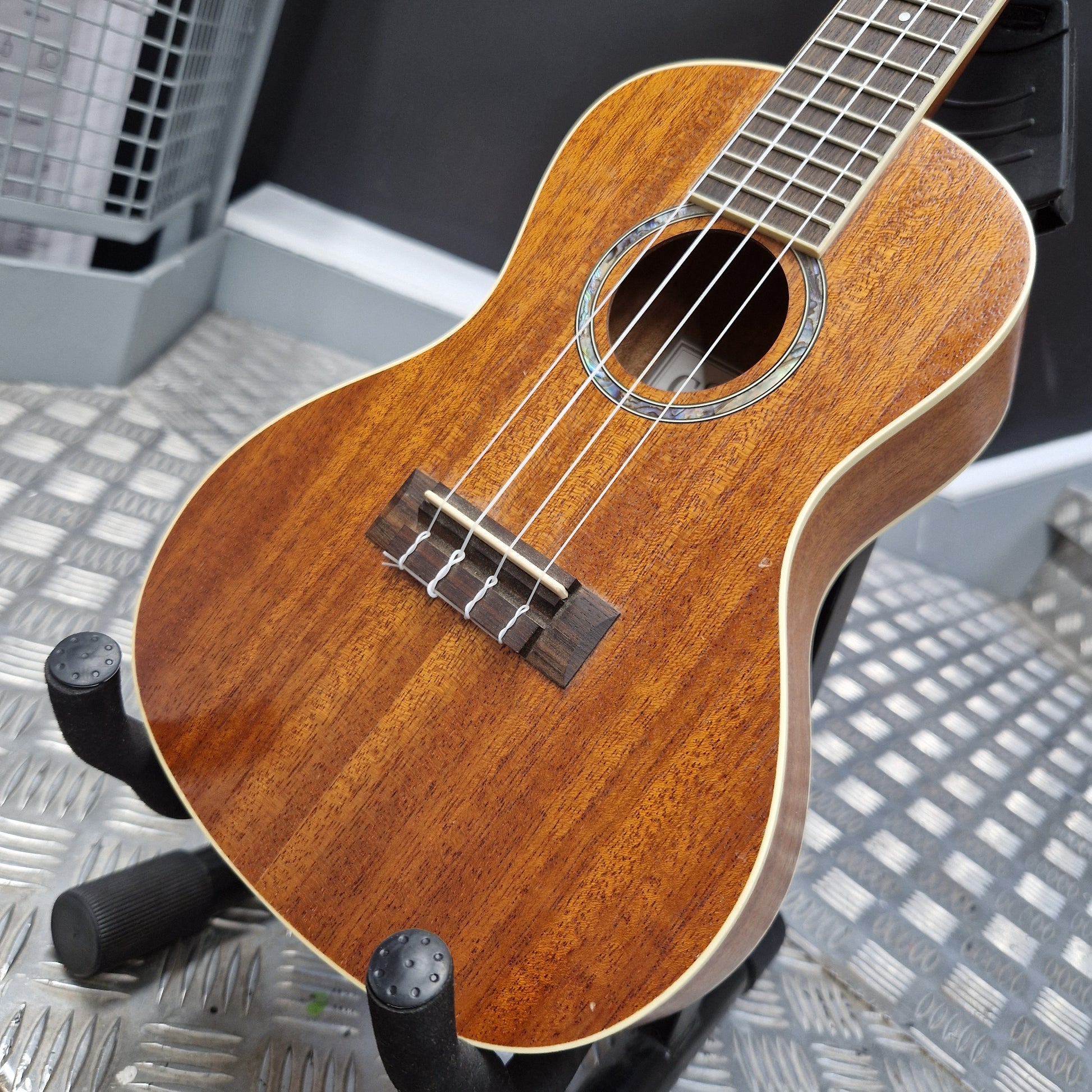 Pre-Owned Cordoba 15CM Wooden ukulele on a stand with a metallic floor background