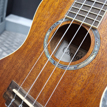 Pre-Owned Cordoba 15CM Close-up of a wooden ukulele with 'Cort' branding on the sound hole.