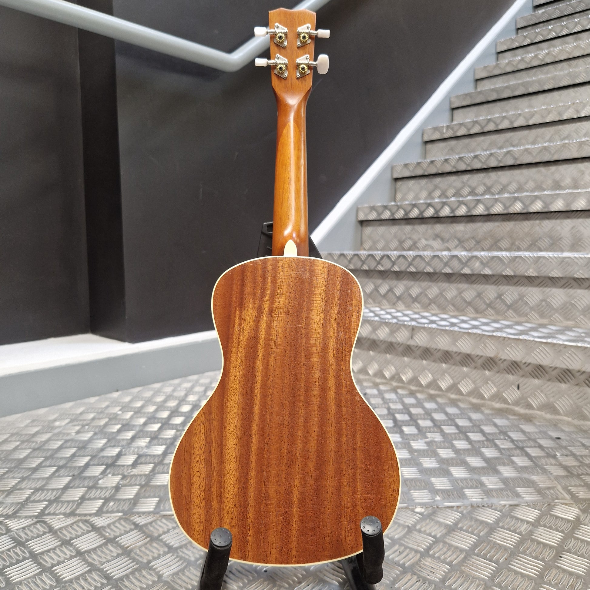 Pre-Owned Cordoba 15CM Wooden ukulele on a stand with a staircase in the background
