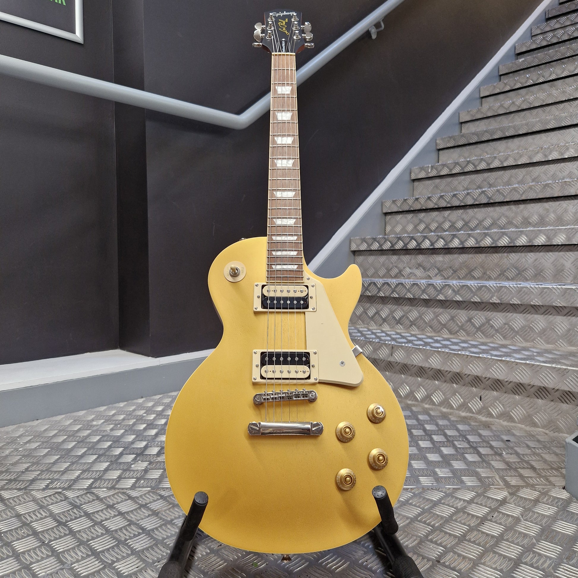 Pre-Owned Epiphone Les Paul yellow electric guitar on a stand with stairs in the background