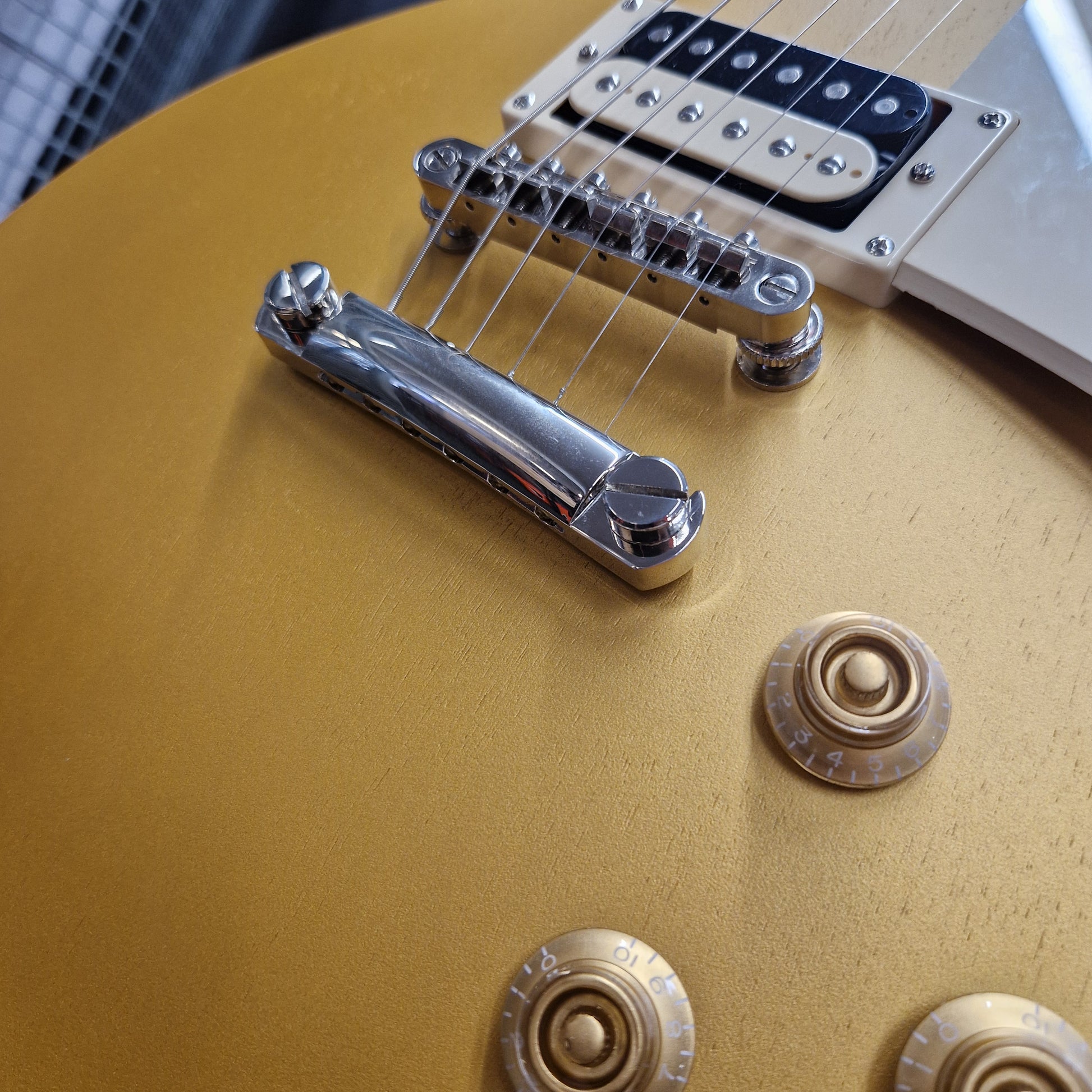 Pre-Owned Epiphone Les Paul Close-up of a gold electric guitar with control knobs and bridge.