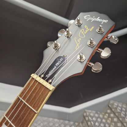 Pre-Owned Epiphone Les Paul Close-up of a guitar headstock with 'Epiphone Les Paul' branding on a blurred background.