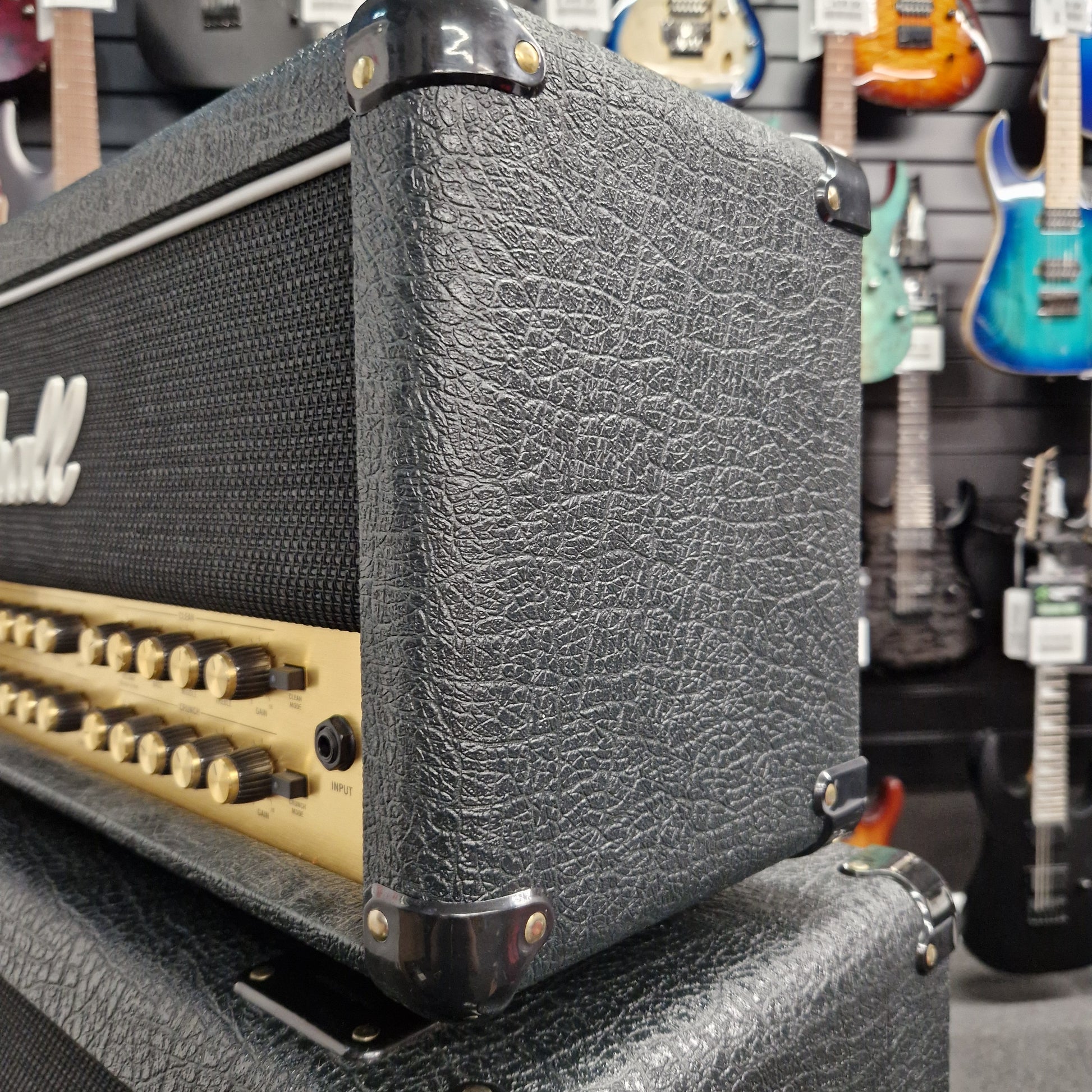 Pre-Owned Marshall JVM410H Close-up of a guitar amplifier with visible brand logo, surrounded by other musical instruments.