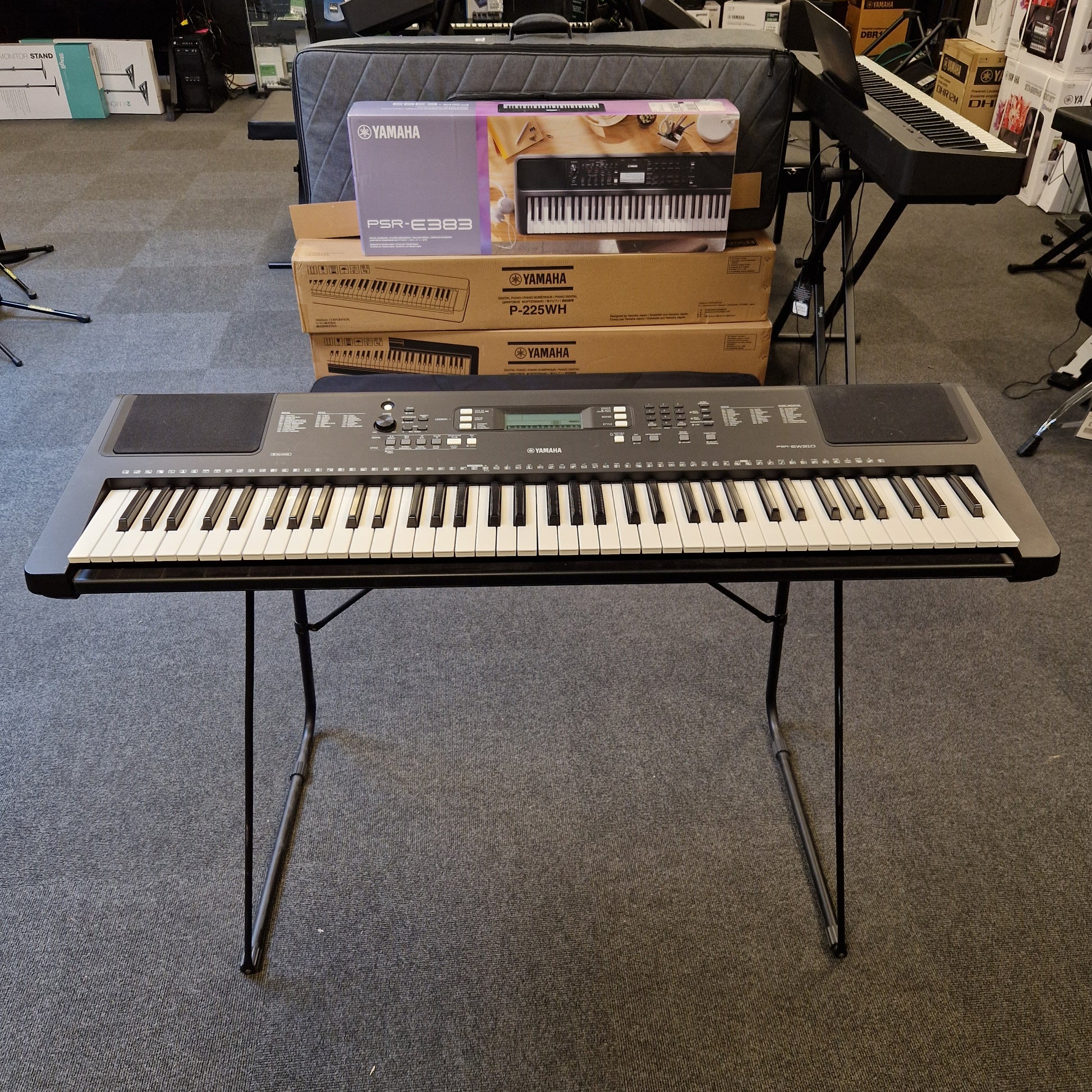 Pre-Owned Yamaha PSR-EW310 Keyboard on a stand with a box of the same keyboard in the background