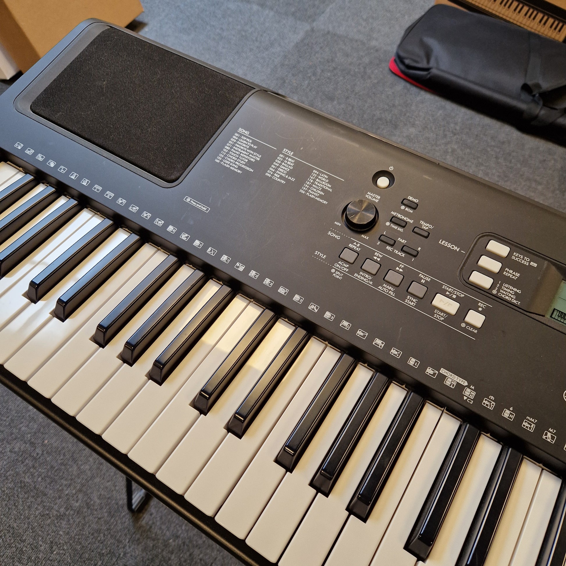 Pre-Owned Yamaha PSR-EW310 Keyboard on a gray surface with a black bag in the background