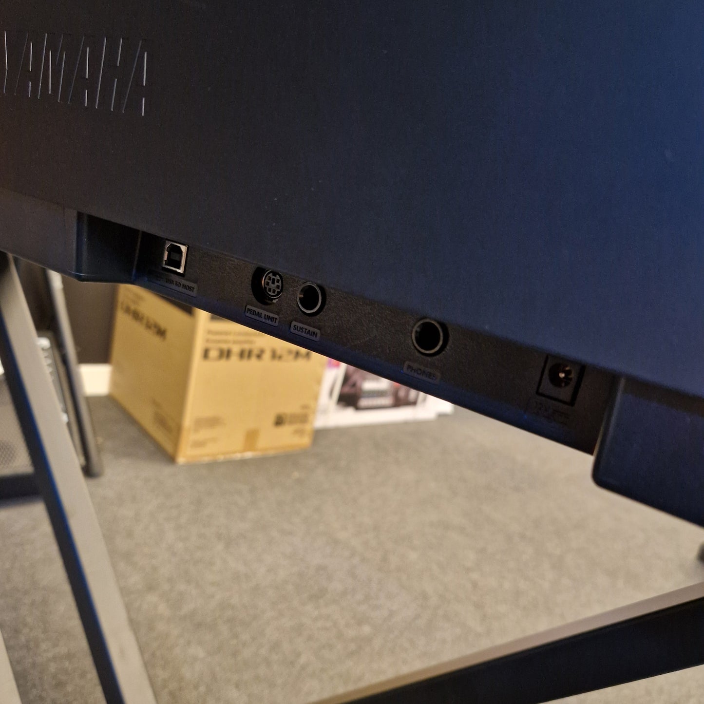 Pre-Owned Yamaha P-145B Back view of a blue electronic device with ports on a reflective surface.