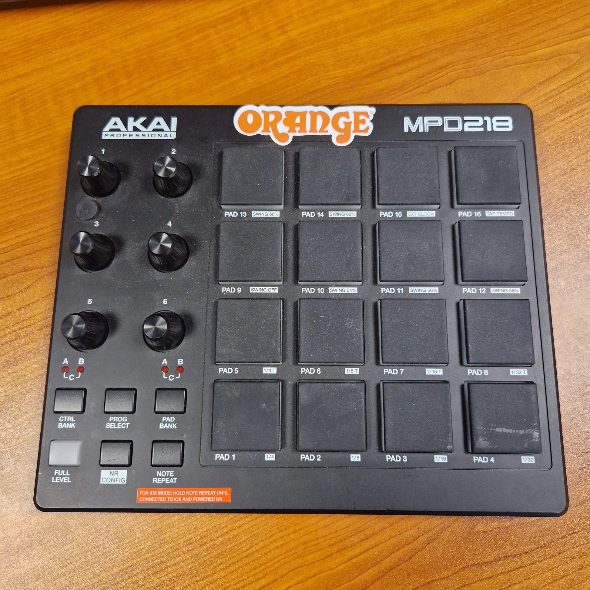Pre-Owned Akai MPD218 Black electronic music controller with 'Orange' and 'Akai' branding on a wooden surface