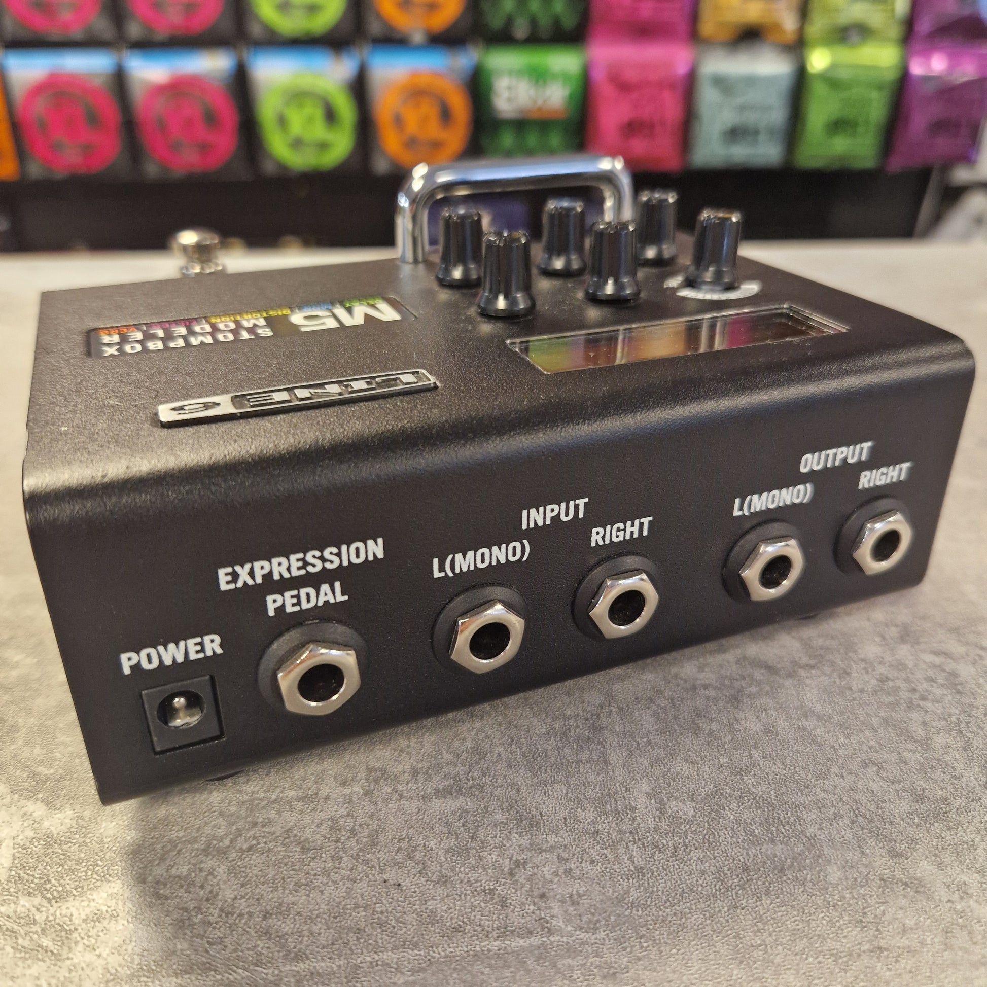 Pre-Owned Line 6 M5 Black expression pedal with various colorful effect pedals in the background