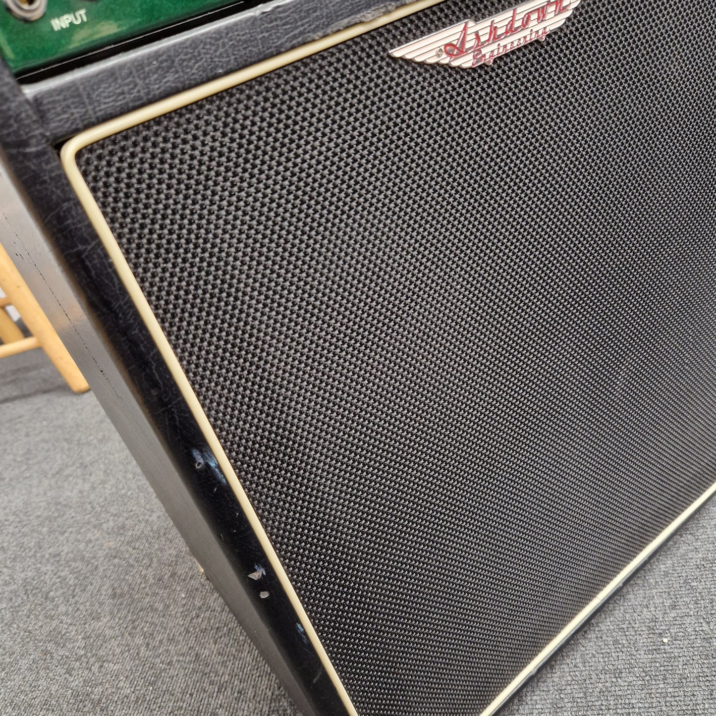 Pre-Owned Ashdown MAG-C210T-300EVO Close-up of a black speaker grill with a brand logo on a gray surface