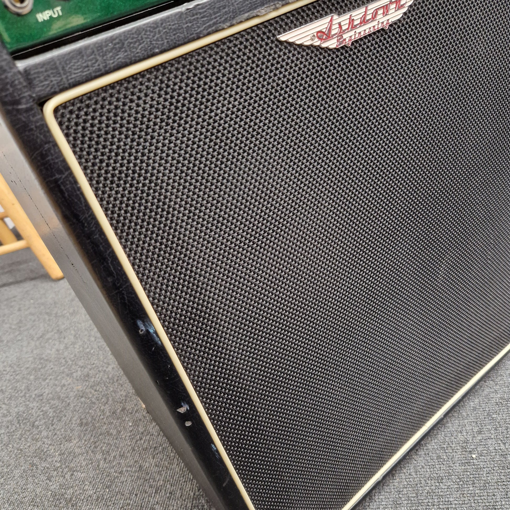 Pre-Owned Ashdown MAG-C210T-300EVO Close-up of a black speaker grill with a brand logo on a gray surface