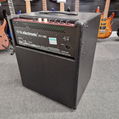 Pre-Owned TC Electronic BG250-112 Black electronic device with 'kc electronic' branding on a gray surface with guitars in the background