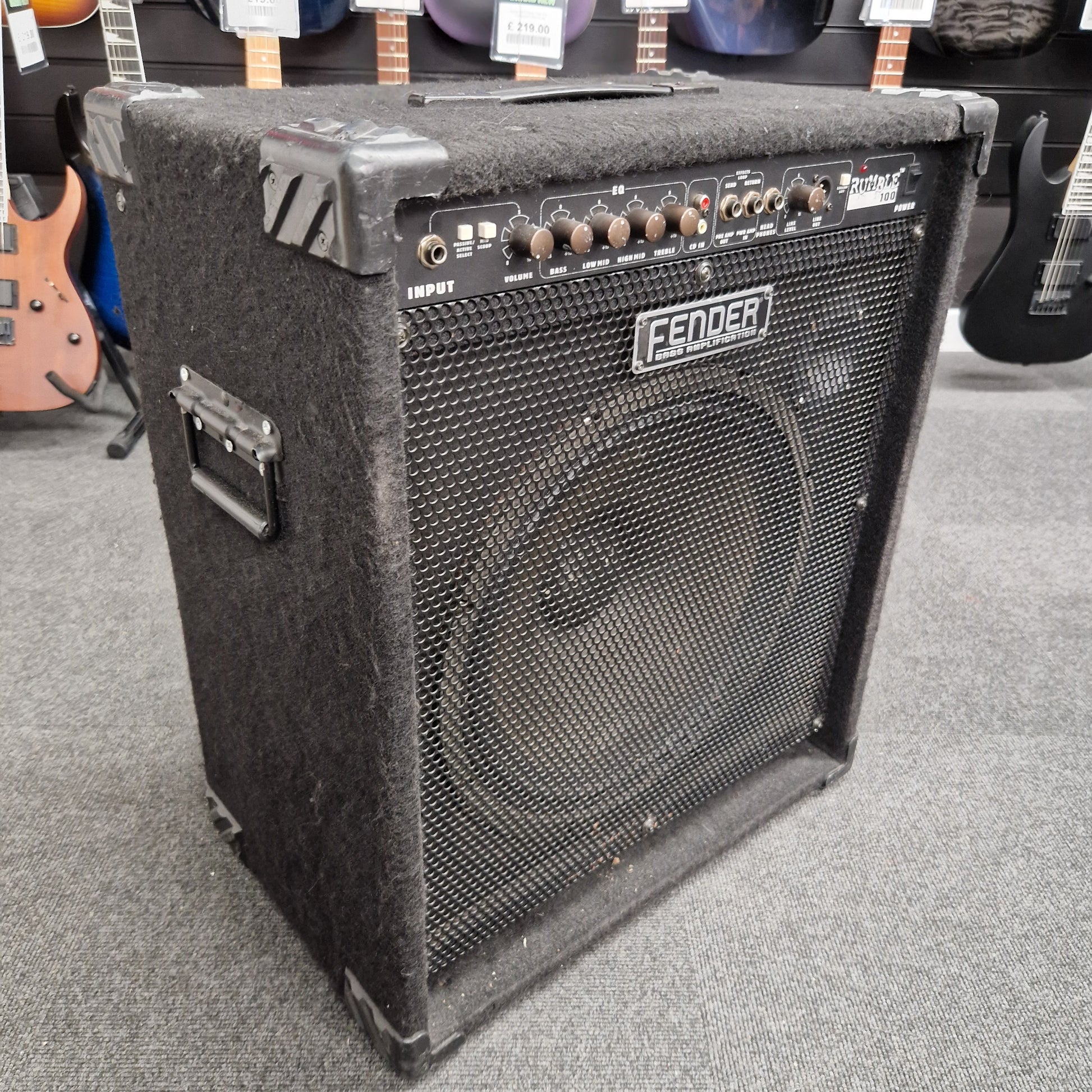 Pre-Owned Fender Rumble 100 Fender guitar amplifier on a gray floor with guitars in the background
