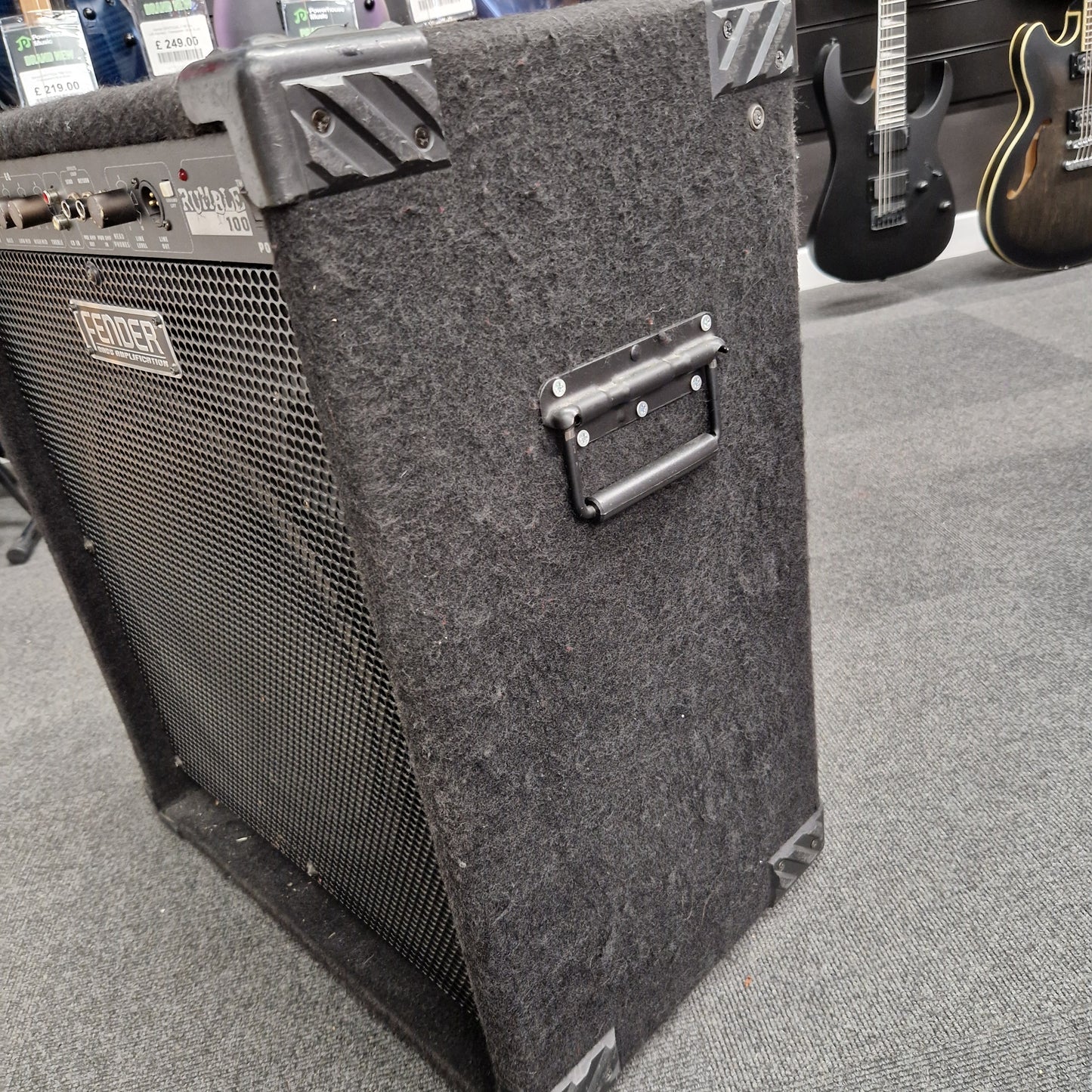 Pre-Owned Fender Rumble 100 Guitar amplifier on a gray floor with guitars in the background