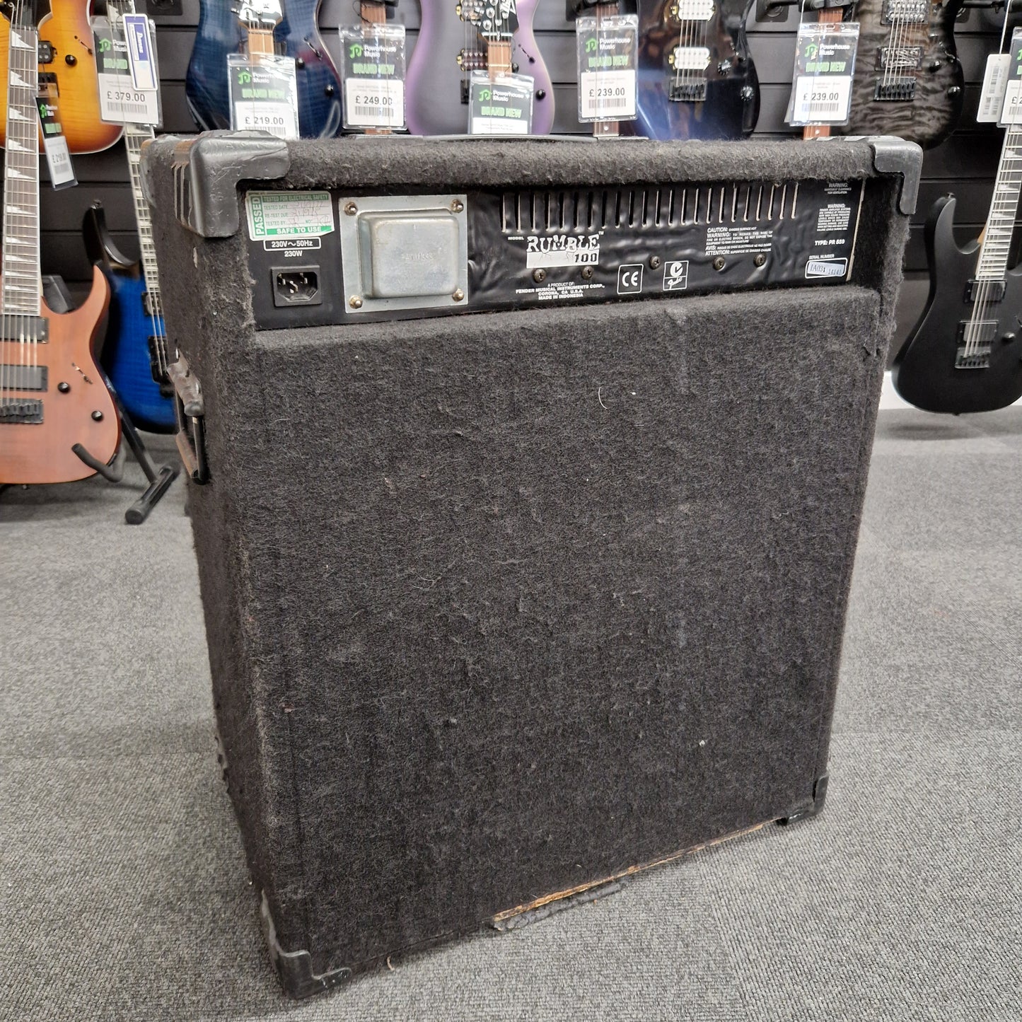 Pre-Owned Fender Rumble 100 Guitar amplifier on a gray floor with guitars in the background