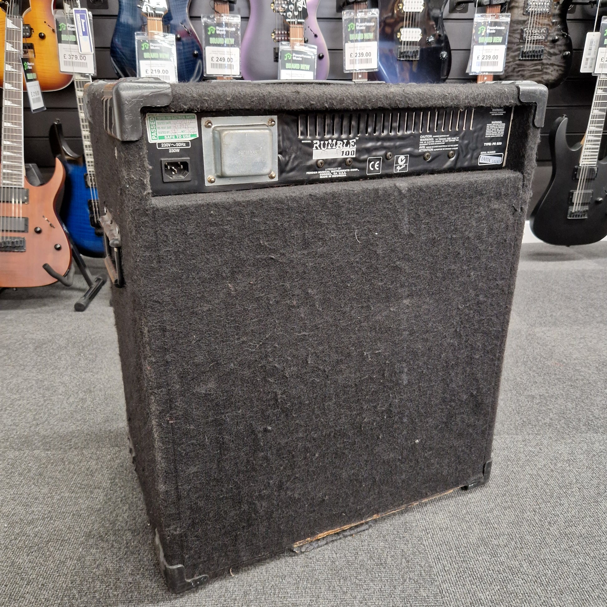 Pre-Owned Fender Rumble 100 Guitar amplifier on a gray floor with guitars in the background