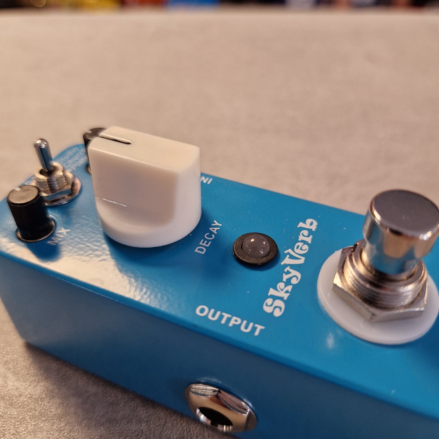 Pre-Owned Mooer MRV2 Blue guitar effects pedal with knobs and labels on a blurred background