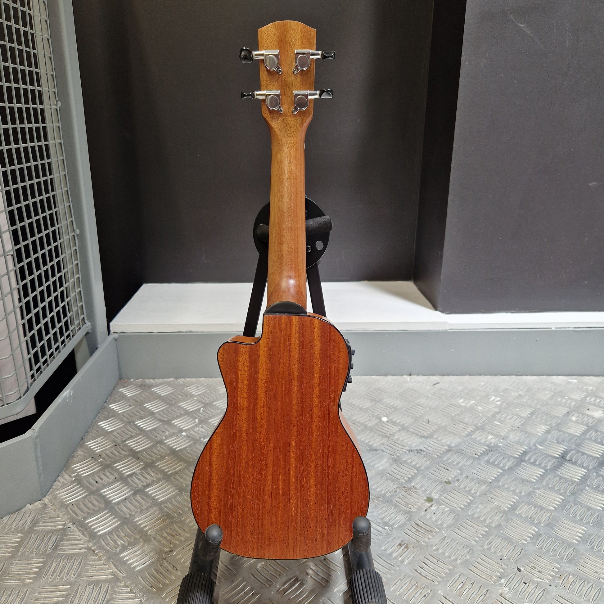 Pre-Owned Alvarez RU26CCE Wooden ukulele leaning against a metal wall.