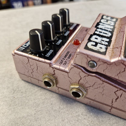 Pre-Owned Digitech Grunge Close-up of a guitar effects pedal with a cracked metallic pinkish-bronze finish, black control knobs, and gold-toned jacks on a light textured surface.