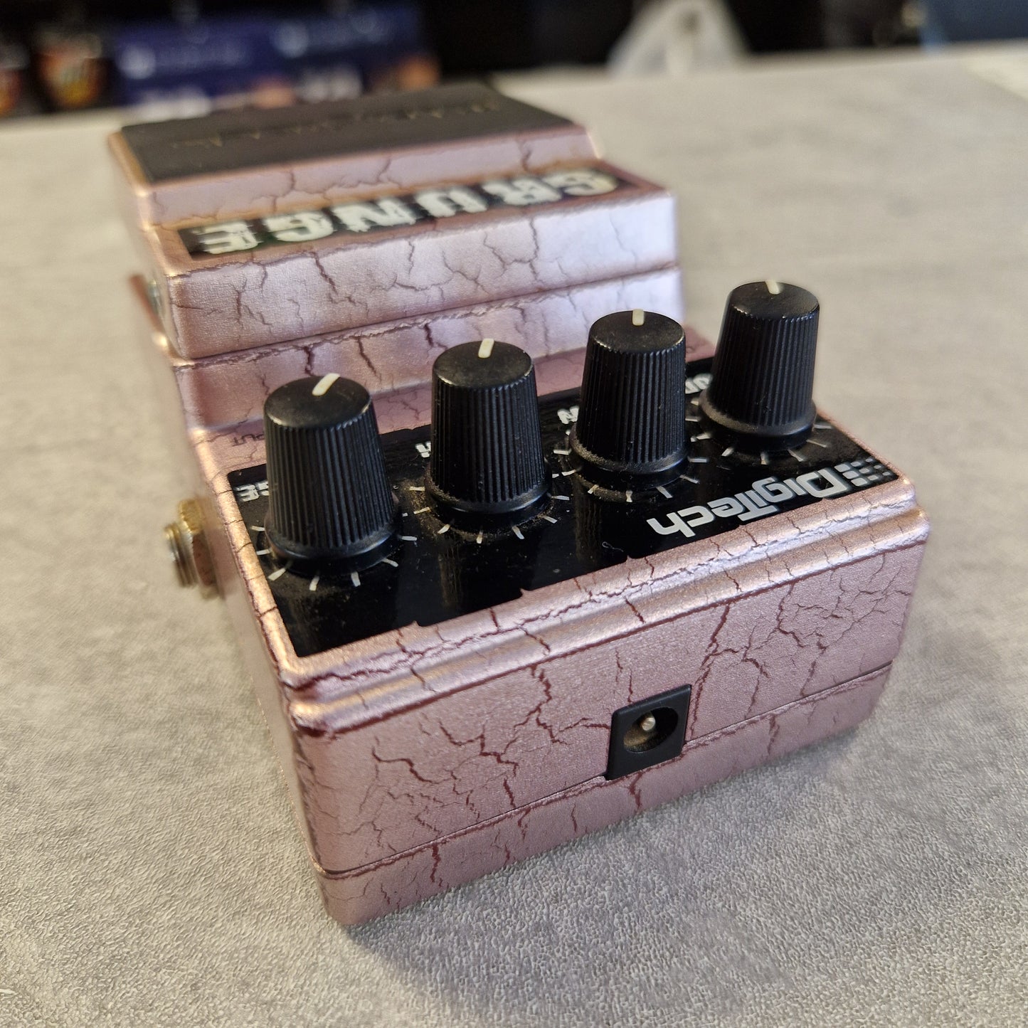 Pre-Owned Digitech Grunge A close-up of a guitar effects pedal with a pinkish-purple cracked metallic finish, four black knobs, and white text reading 'Grumble' and 'Sodapalm'.