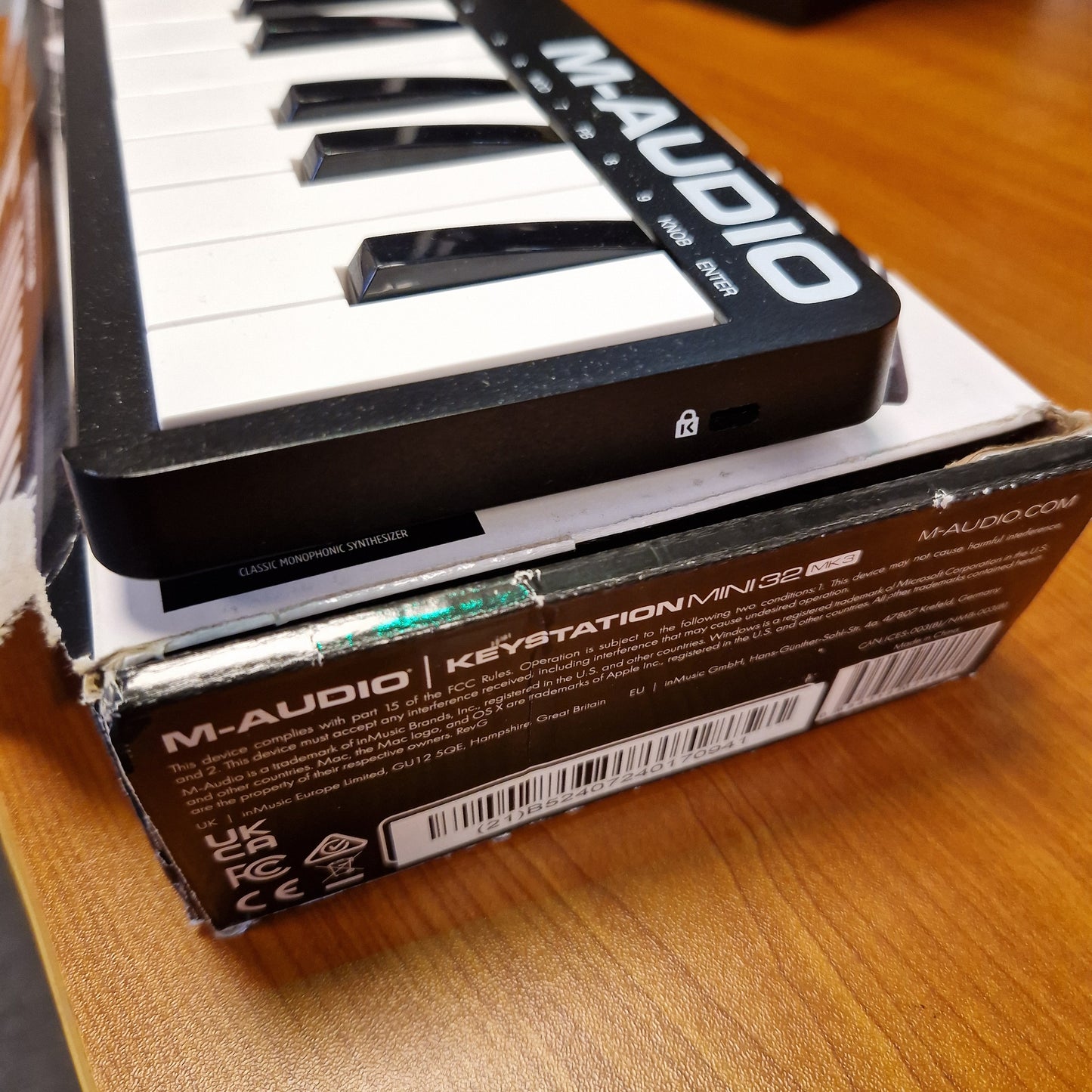 Pre-Owned M-Audio Keystation M-Audio Kaveration Mini 16-key MIDI controller next to its original retail box on a wooden surface.