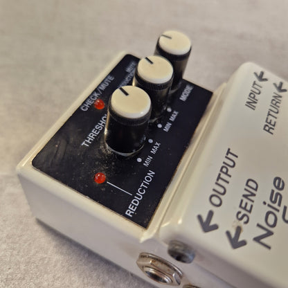 Pre-Owned Boss NS-2  A close-up of a white and black noise gate pedal with three control knobs, labeled with input/output/send, mode, threshold, check/route, reduction, and min/max settings.