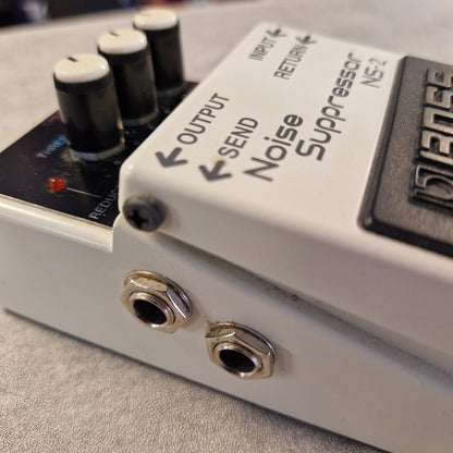 Pre-Owned Boss NS-2  Close-up of a Boss NS-2 Noise Suppresser guitar pedal showing the white control panel, black knobs, silver jacks, and printed control labels.