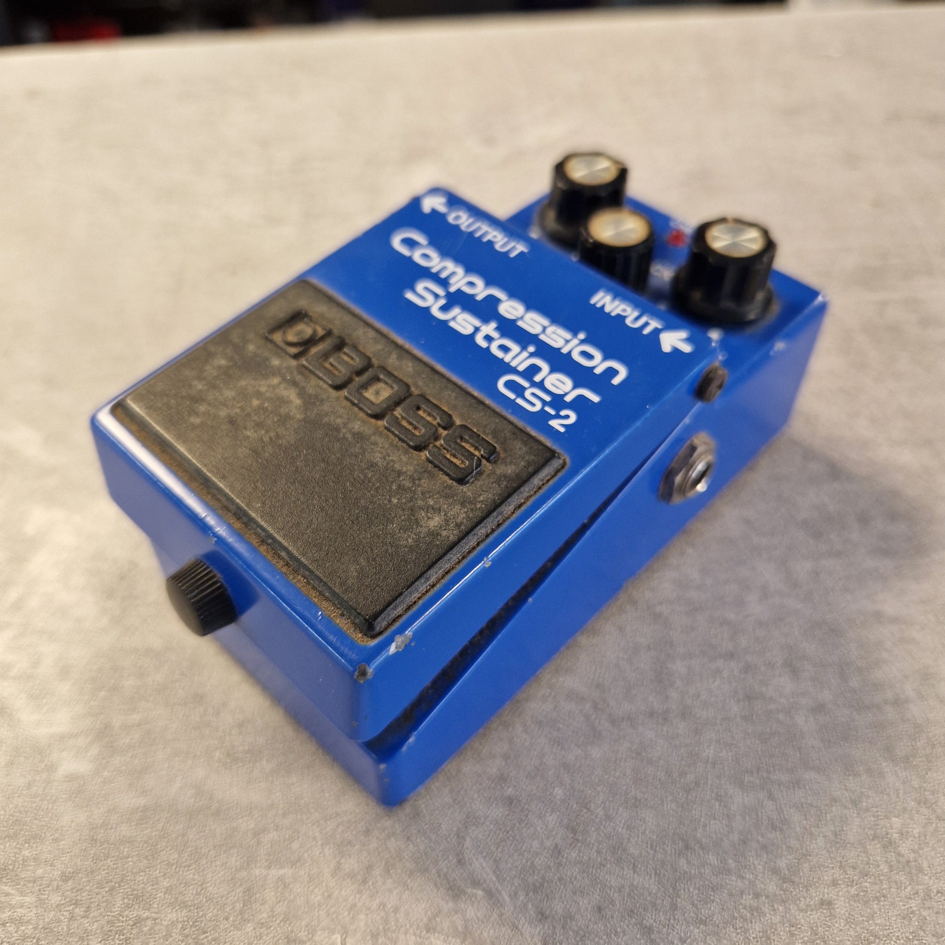 Pre-Owned Boss CS-2 A blue Boss CS-2 compression sustainer guitar pedal with black knobs and a black footswitch plate, photographed on a textured gray surface.