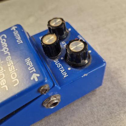 Pre-Owned Boss CS-2 A blue compression driver guitar pedal with black knobs and white text, photographed close-up against a gray textured background.