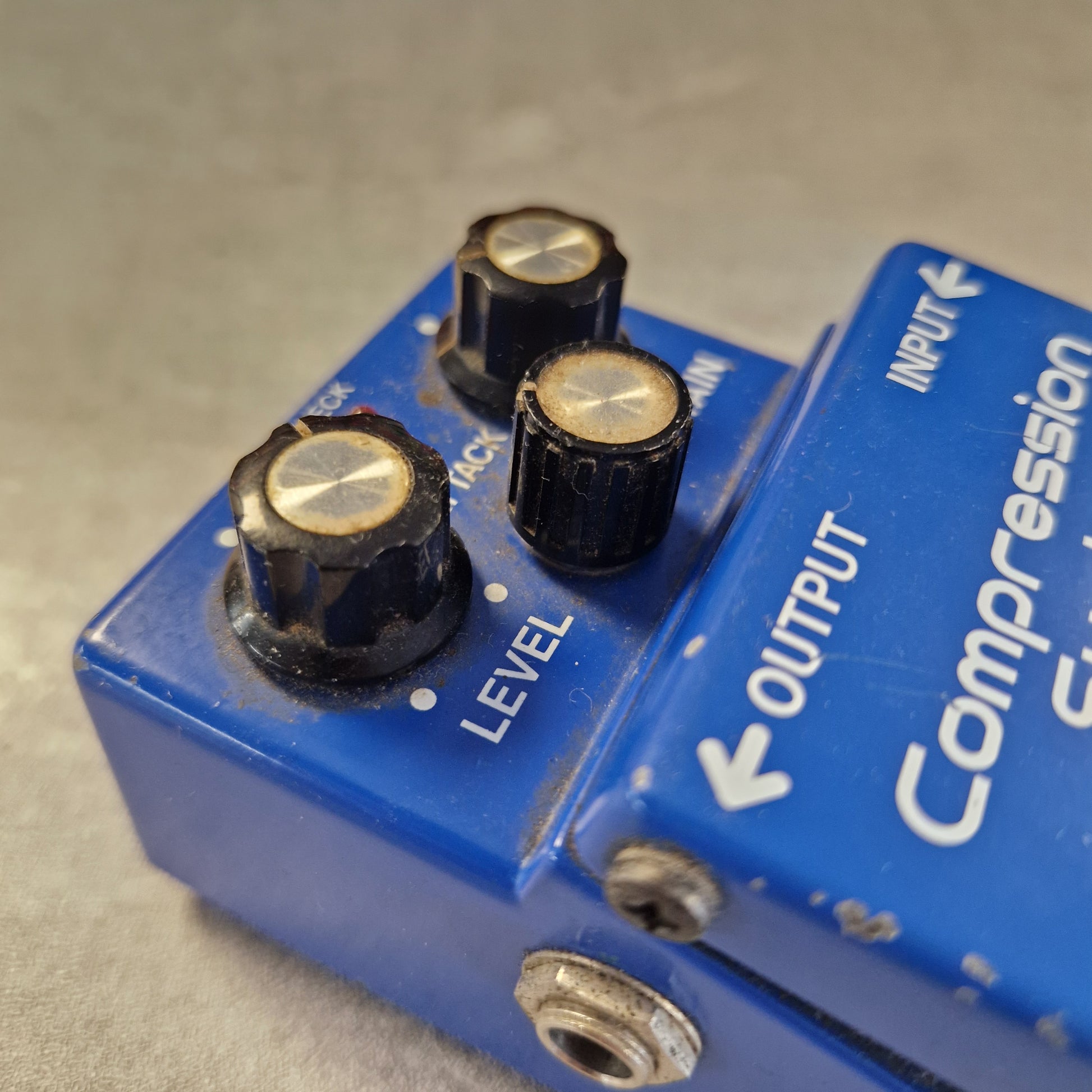 Pre-Owned Boss CS-2 A close-up of a blue compression guitar pedal with black knobs and white printed labels, photographed on a light gray surface.