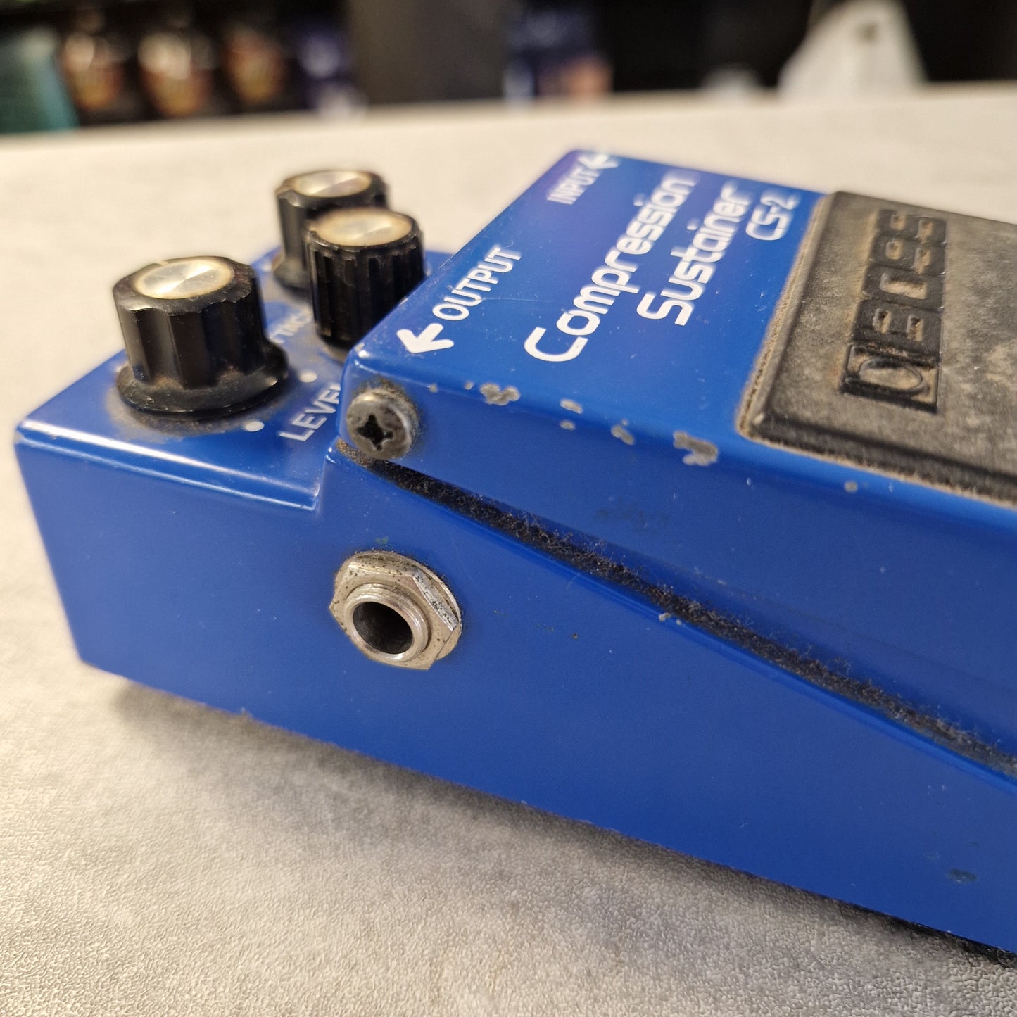 Pre-Owned Boss CS-2 A close-up of a blue Boss CS-2 compression pedal with black knobs and white text, photographed against a light gray textured background.