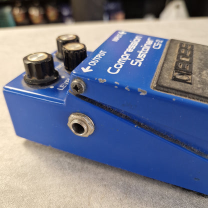 Pre-Owned Boss CS-2 A close-up of a blue Boss CS-2 compression pedal with black knobs and white text, photographed against a light gray textured background.