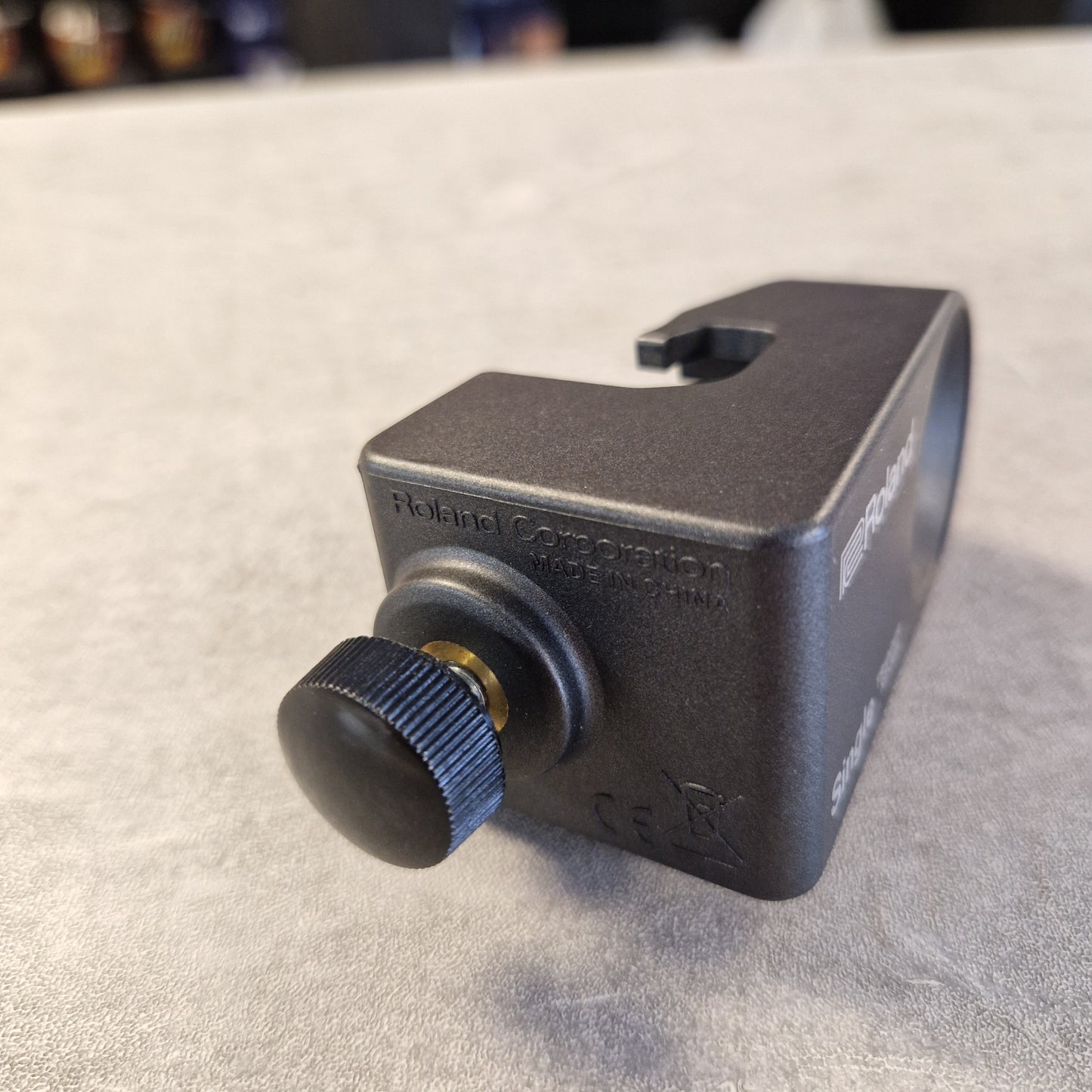 Pre-Owned Roland RT-30H A close-up of a black metal camera lens filter or lens body component with a knurled adjustment knob, photographed against a textured light gray surface.