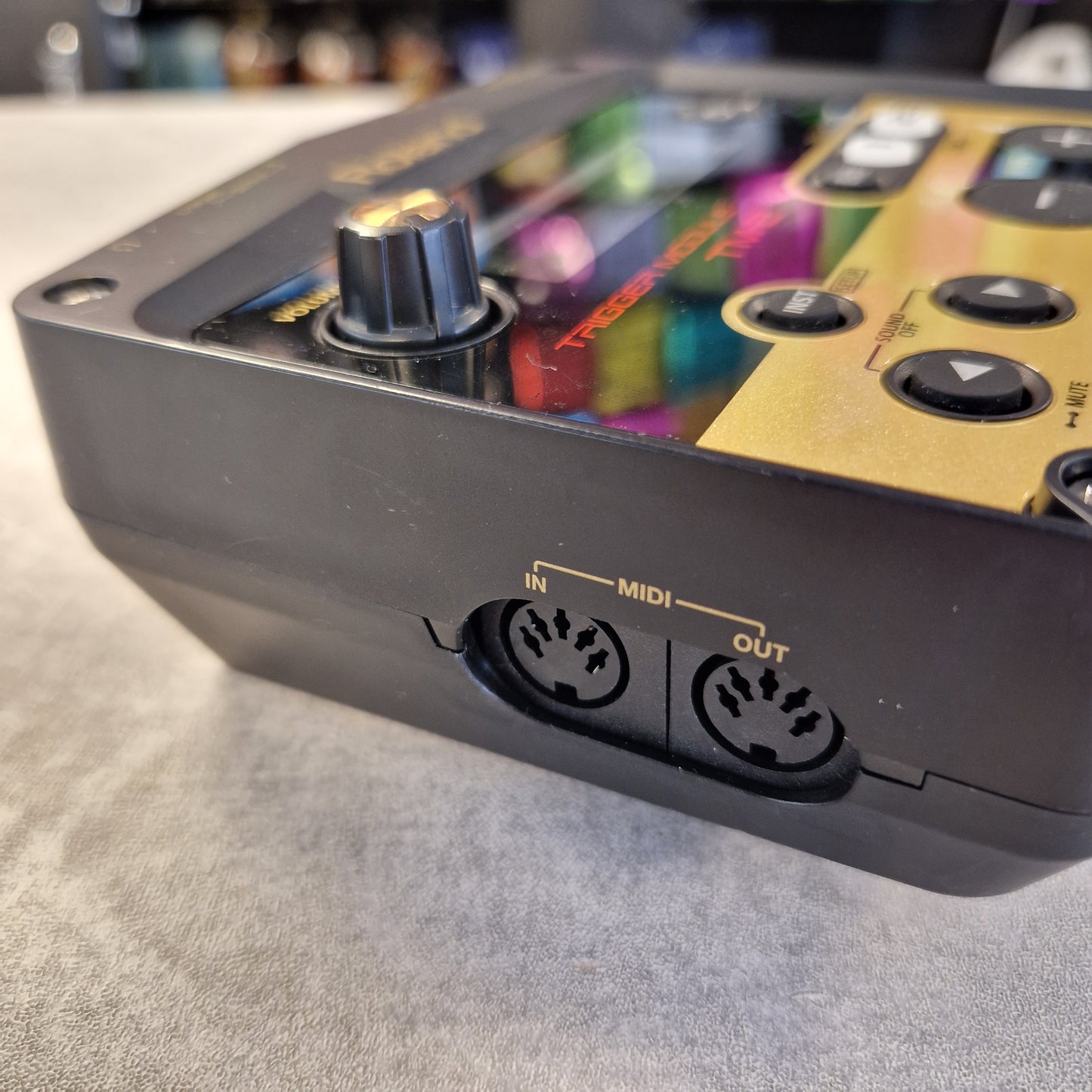 Pre-Owned Roland TM-2 Close-up of a black electronic music controller showing MIDI input and output jacks, with a gold panel and colorful display screen.